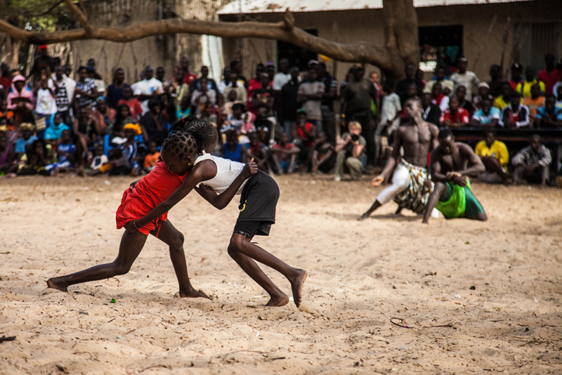 “ La lutte est notre premier jeu, avant le football”, dit Karafa Diatta, à la tête du comité de lutte du festival. Léna, 5 ans, et Angèle 7 ans, partagent l’arène avec des lutteurs poids lourds. Lors du festival, tout le monde est invité à entrer dans l’arène. 