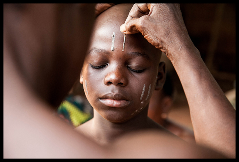 Après les deux jours de cérémonie, chaque parent décide ou non si les enfants traverseront aussi la dernière étape, celle de la scarification. “Aujourd’hui, ce n’est plus obligatoire, assure le vigan. On n’oblige plus personne.” Mais les parents d’Hospice (photo), Luc et Marina ont déjà pris leur décision. Dans la cour de chez Gamba Dahoui, “coupeuse” depuis des années, on met de la cendre sur les endroits du visage qui doivent recevoir les entailles. 